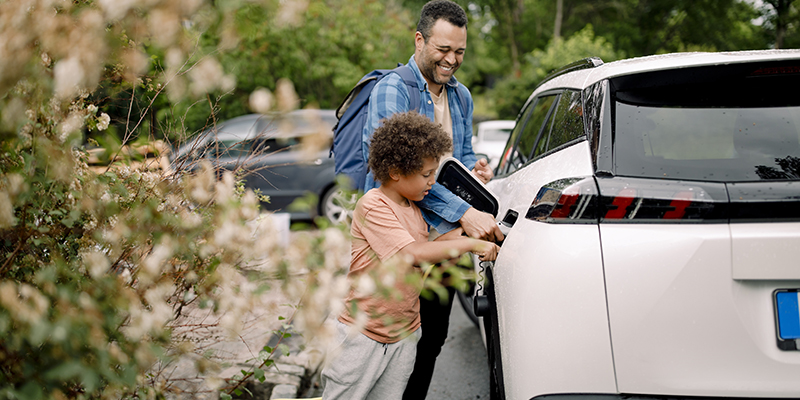 A dad showing his son how to recharge an electric vehicle by plugging the charger into the car.